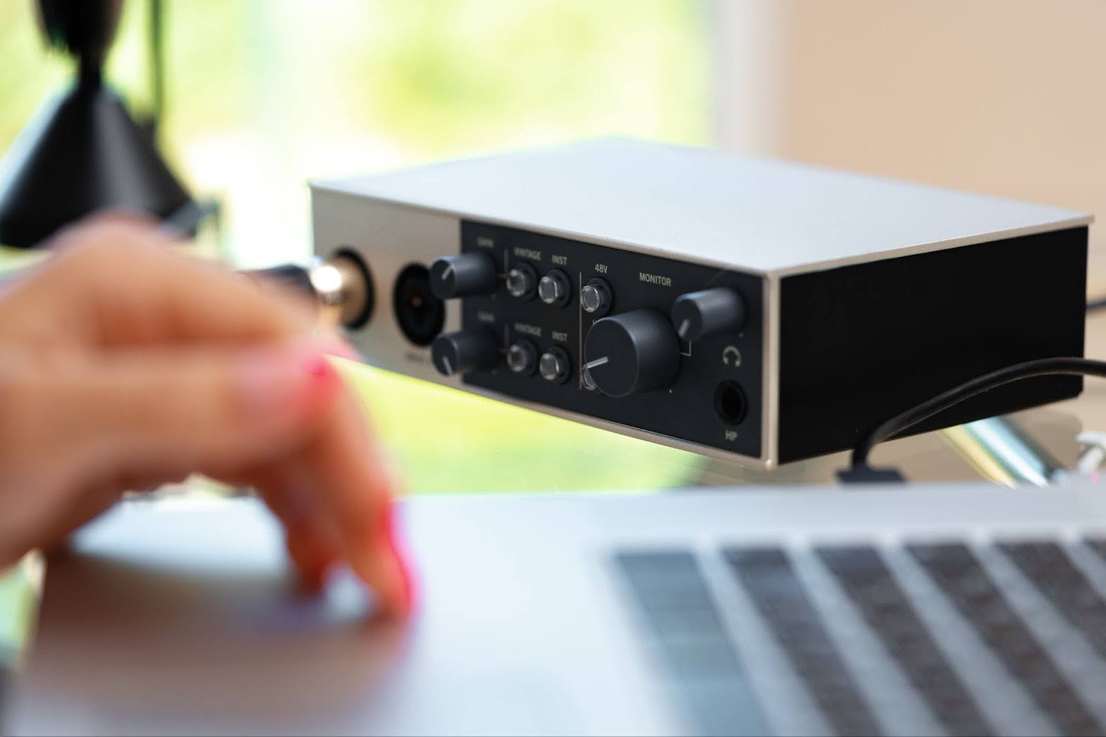 Image of a woman's hand on a laptop trackpad with an audio interface in the background.