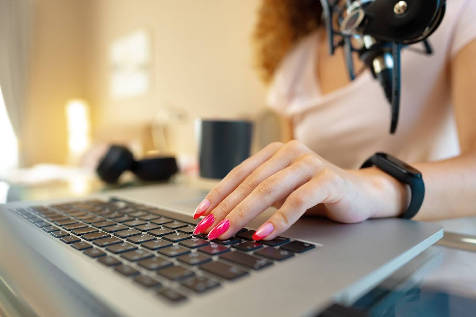 Image of a woman's hand typing on a laptop with a microphone in front of her.