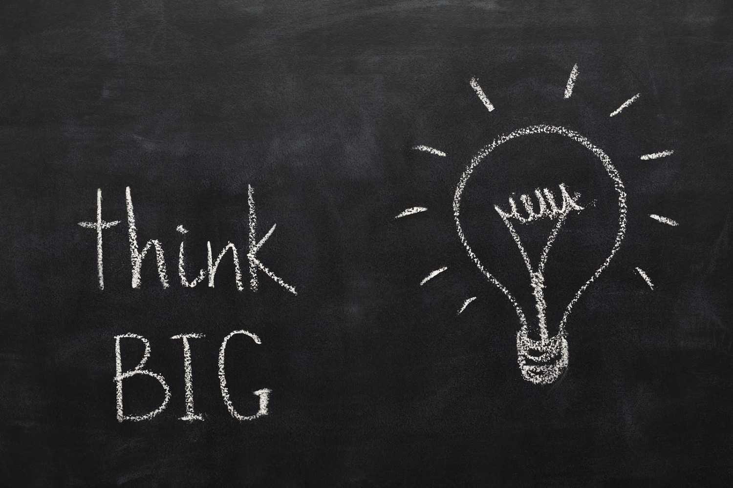 A blackboard with "think big" and a drawing of a lightbulb in white chalk