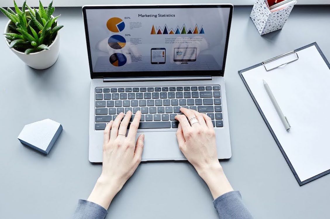 Image of a woman's hands typing on a laptop with marketing statistics on the screen