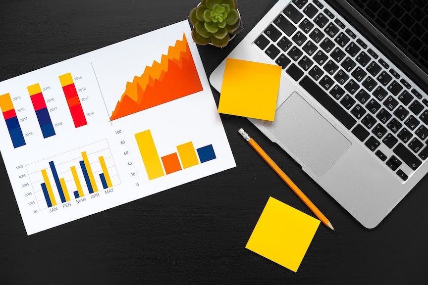 Image of a laptop on paperwork with graphs and data on a table