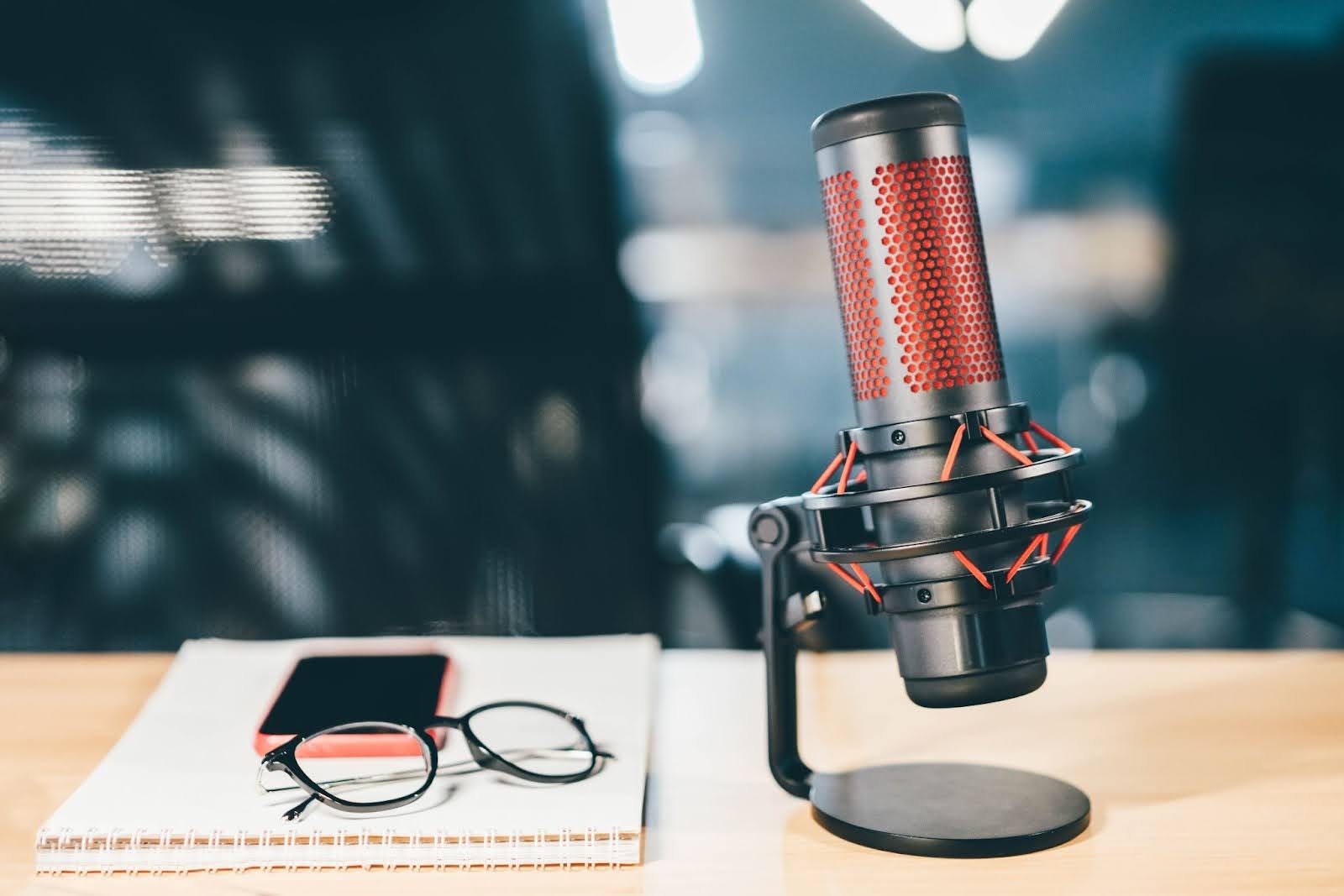 Image of a podcasting microphone, notebook, phone, and glasses on a table.