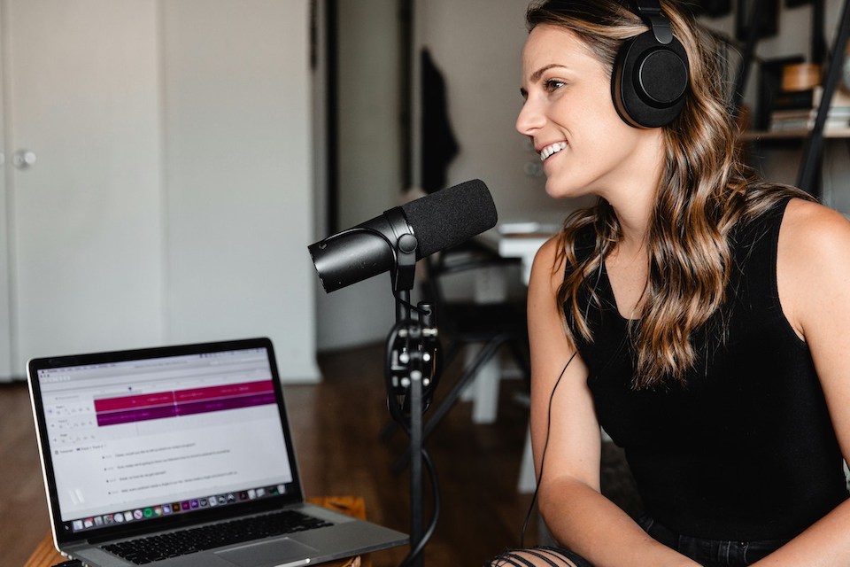 Woman in black top sitting in front of a laptop recording a podcast