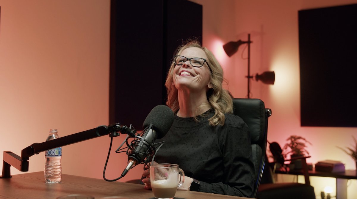 Image of a woman smiling in front of a microphone in a podcast recording studio