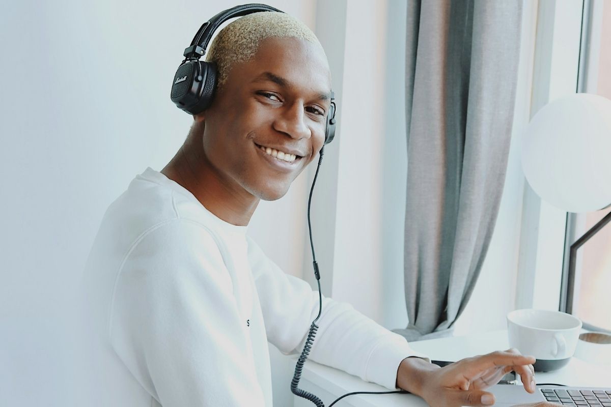 Person in a white long sleeve shirt with black headphones on smiling at the camera