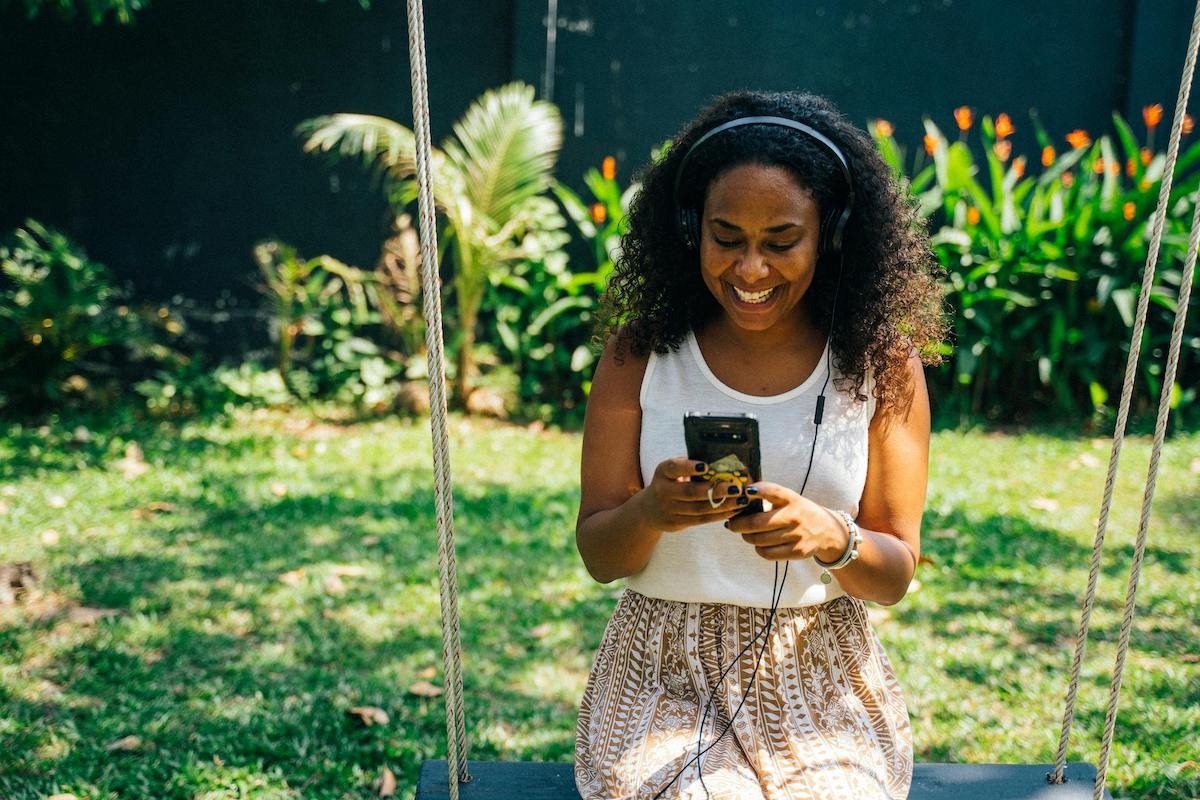 A woman on a swing chair listening to a podcast on her phone